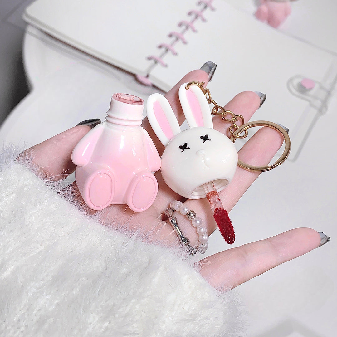 Pink and white bunny-shaped lip balm with a keychain on a hand against a white background