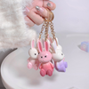 Three colorful rabbit-shaped keychains on a gold chain held by a hand.