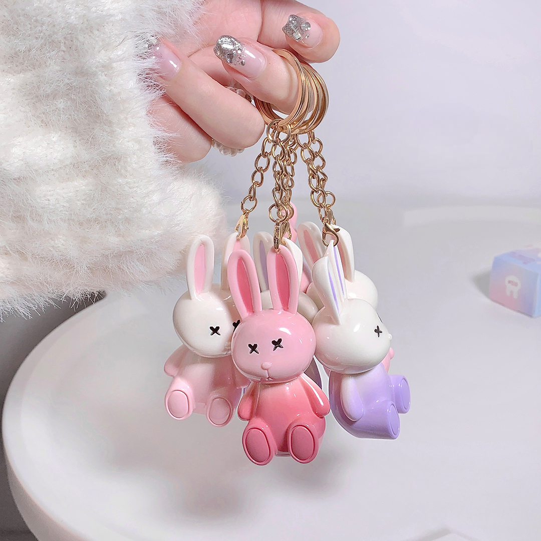 Three colorful rabbit-shaped keychains on a gold chain held by a hand.