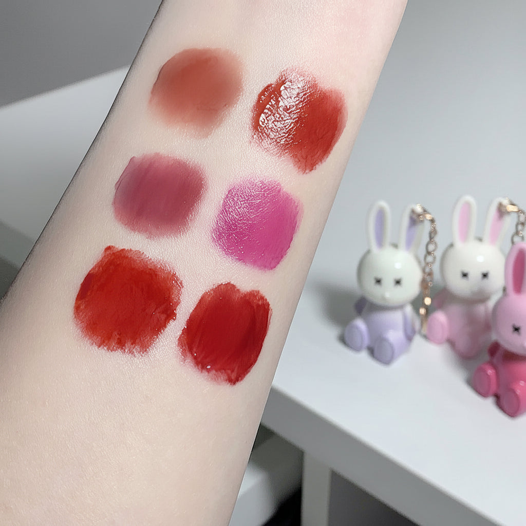 Lipstick swatches on a person's arm with small rabbit figurines in the background.