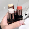 Three makeup sticks with different shades held by a hand against a neutral background
