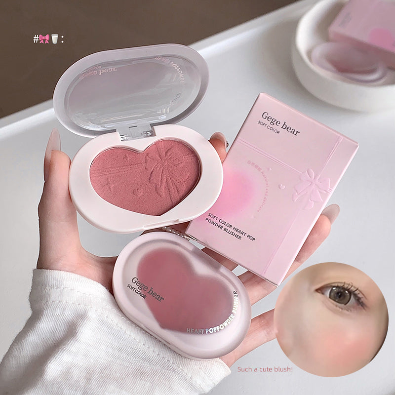 Heart-shaped blush compact with packaging held by a hand, on a neutral background.