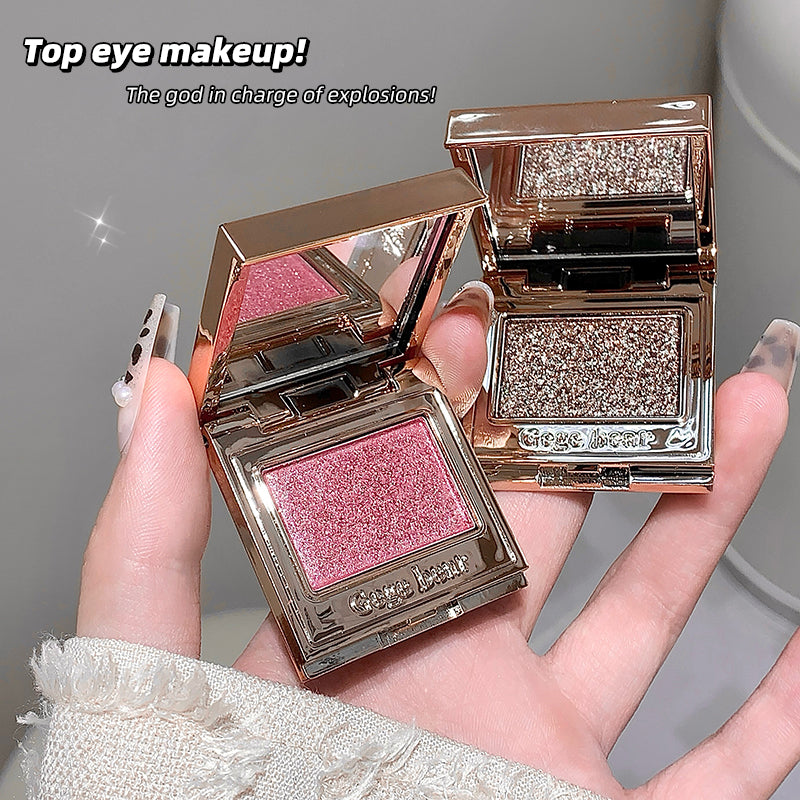 Two open makeup compact cases with pink and glittery contents held in a hand against a neutral background.
