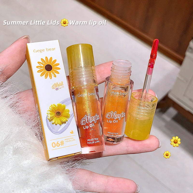 Two bottles of 'Magic Lip Oil' held by a hand with a box labeled 'Gige bear' on a light background.