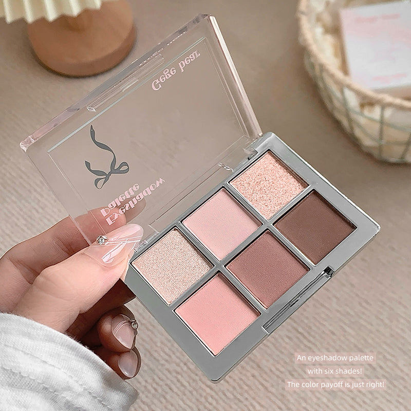 Makeup eyeshadow palette with six shades held by a hand on a neutral background