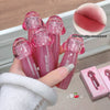Hand holding pink lip glosses with a close-up of a lip and text on a wooden surface.