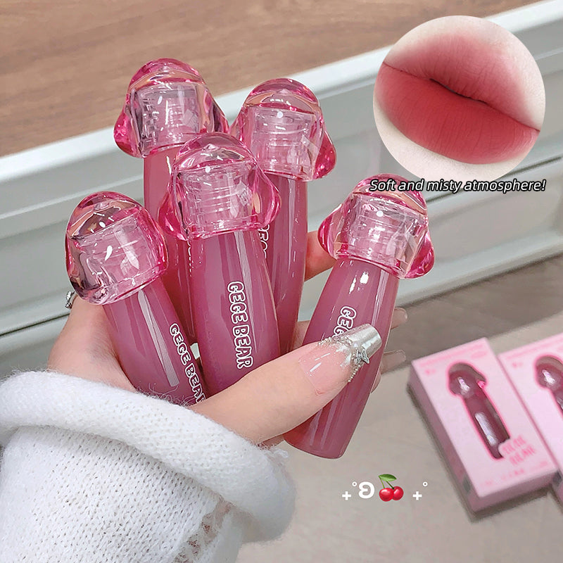 Hand holding pink lip glosses with a close-up of a lip and text on a wooden surface.