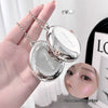 Silver compact mirror held in a hand with a close-up of a face and text overlay.