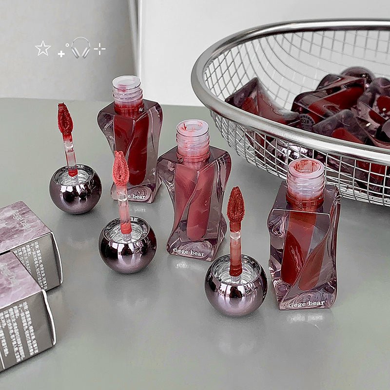 Red nail polish bottles with application tips on a light gray surface, with a basket of red items in the background.