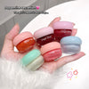 Hand holding six small jars of 'Gege bear' lip balm in various colors on a white surface.