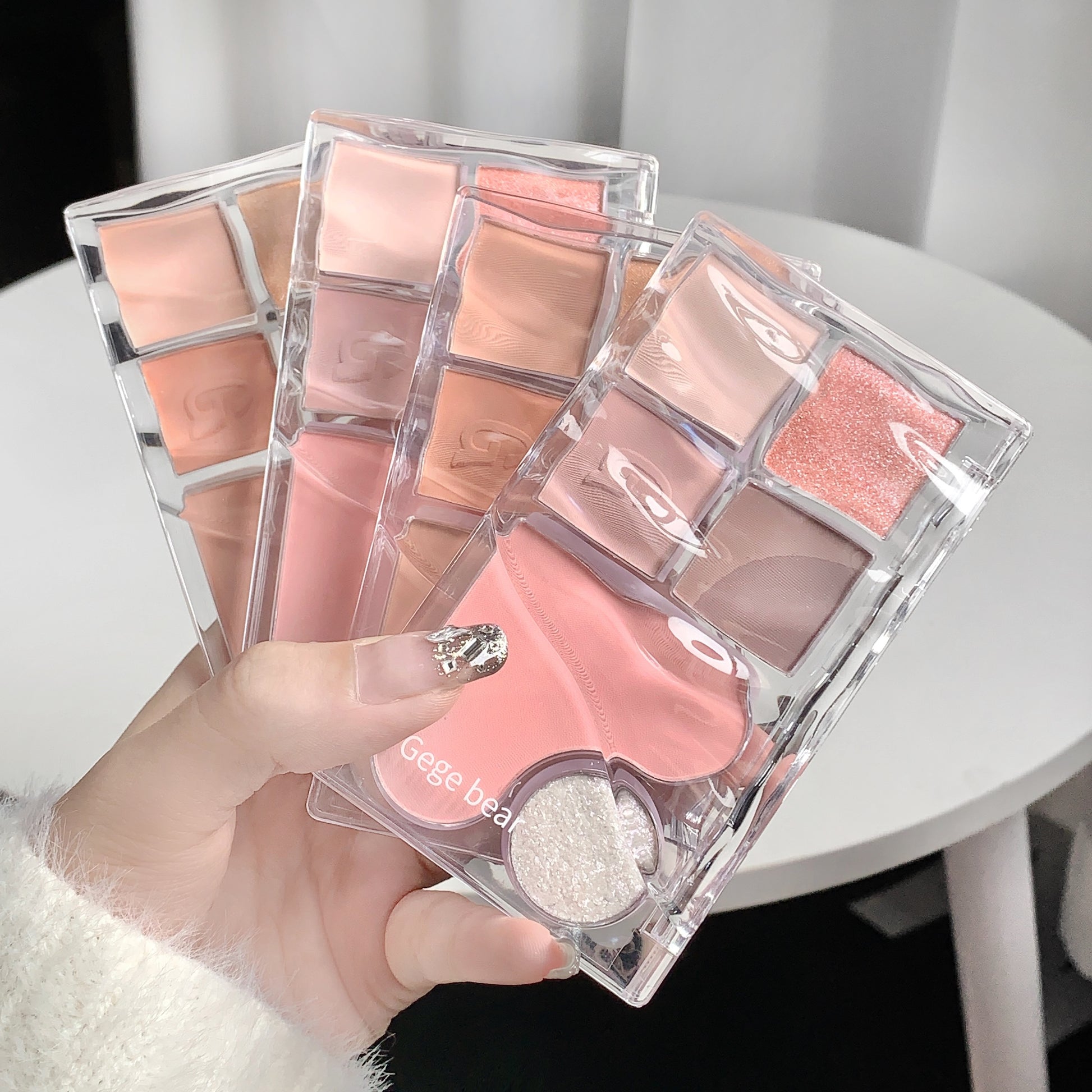 Makeup palette with pink shades held by a hand on a white surface