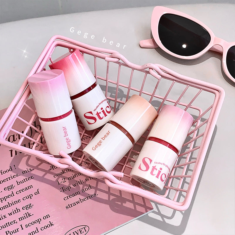 Four cosmetic bottles with 'Stic' branding on a pink wire basket, next to sunglasses.