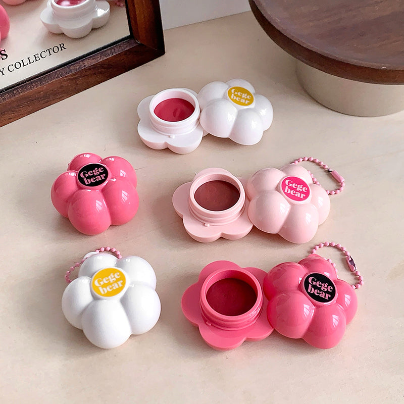 Set of pink and white flower-shaped lip balm containers on a beige surface.