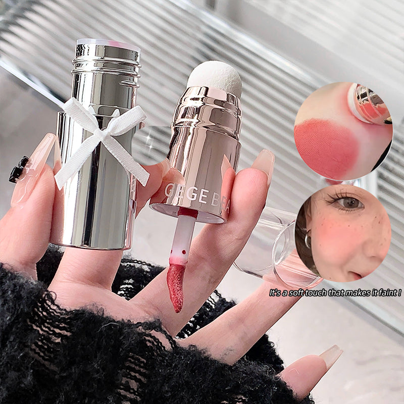 Silver makeup brush and pink lip gloss held by a hand, with a close-up of the lip gloss and a person wearing it.