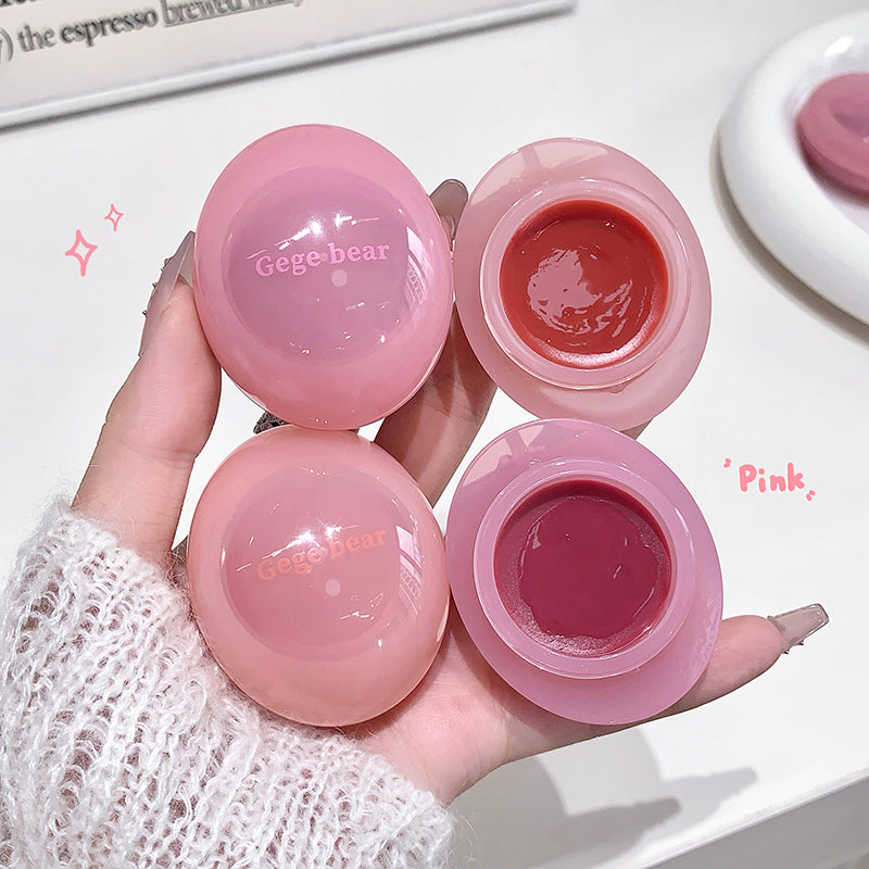 Pink lip balm containers with visible brand name held by a hand on a light background.