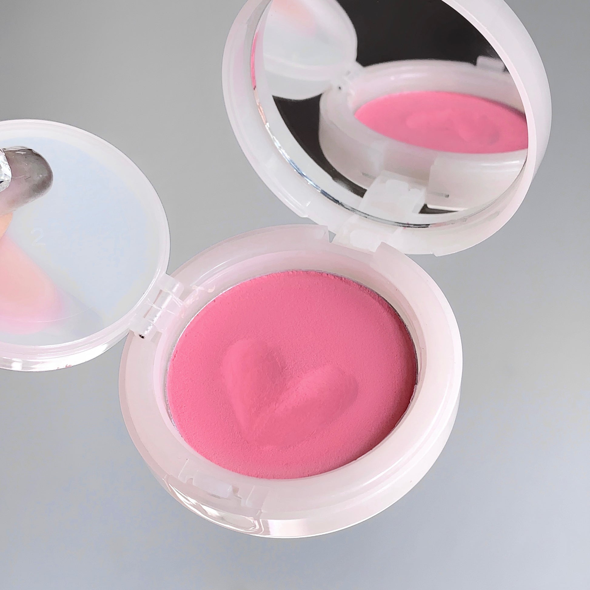 Compact with pink blush on a gray background
