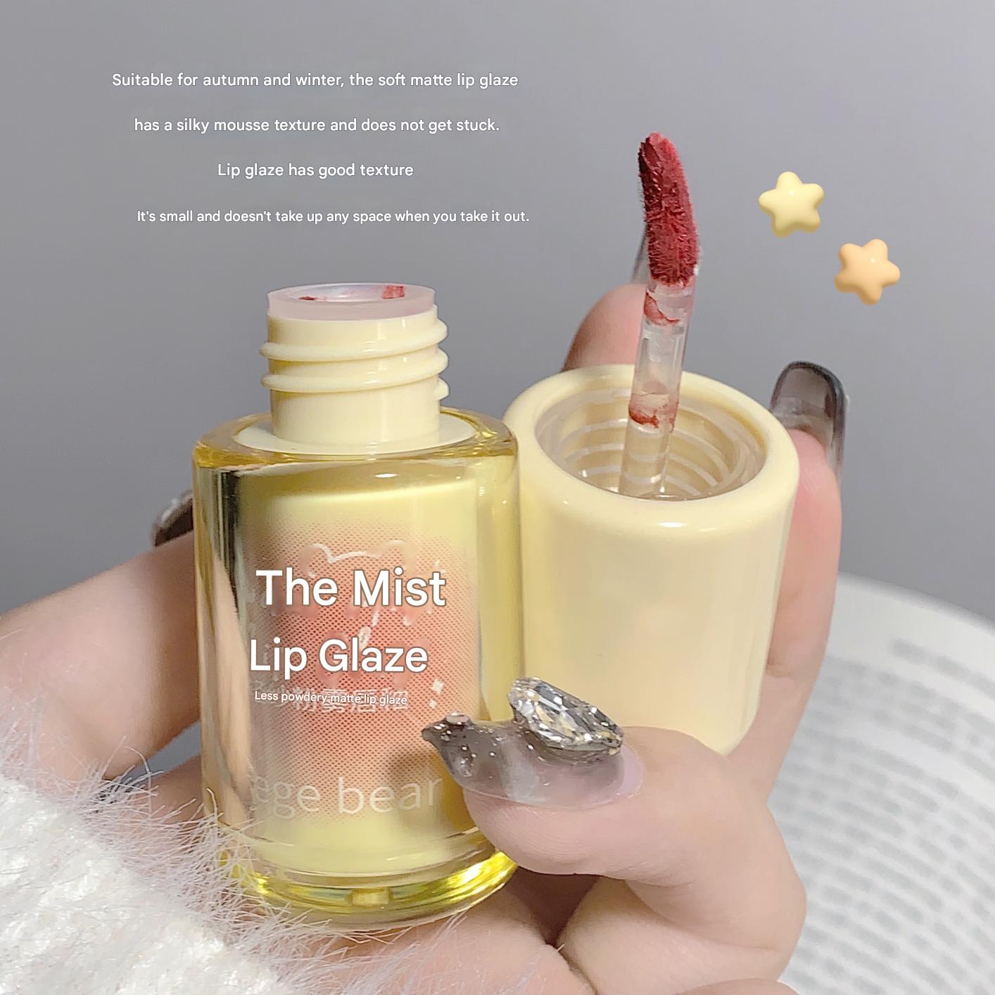 Lip glaze with applicator held by a hand against a gray background