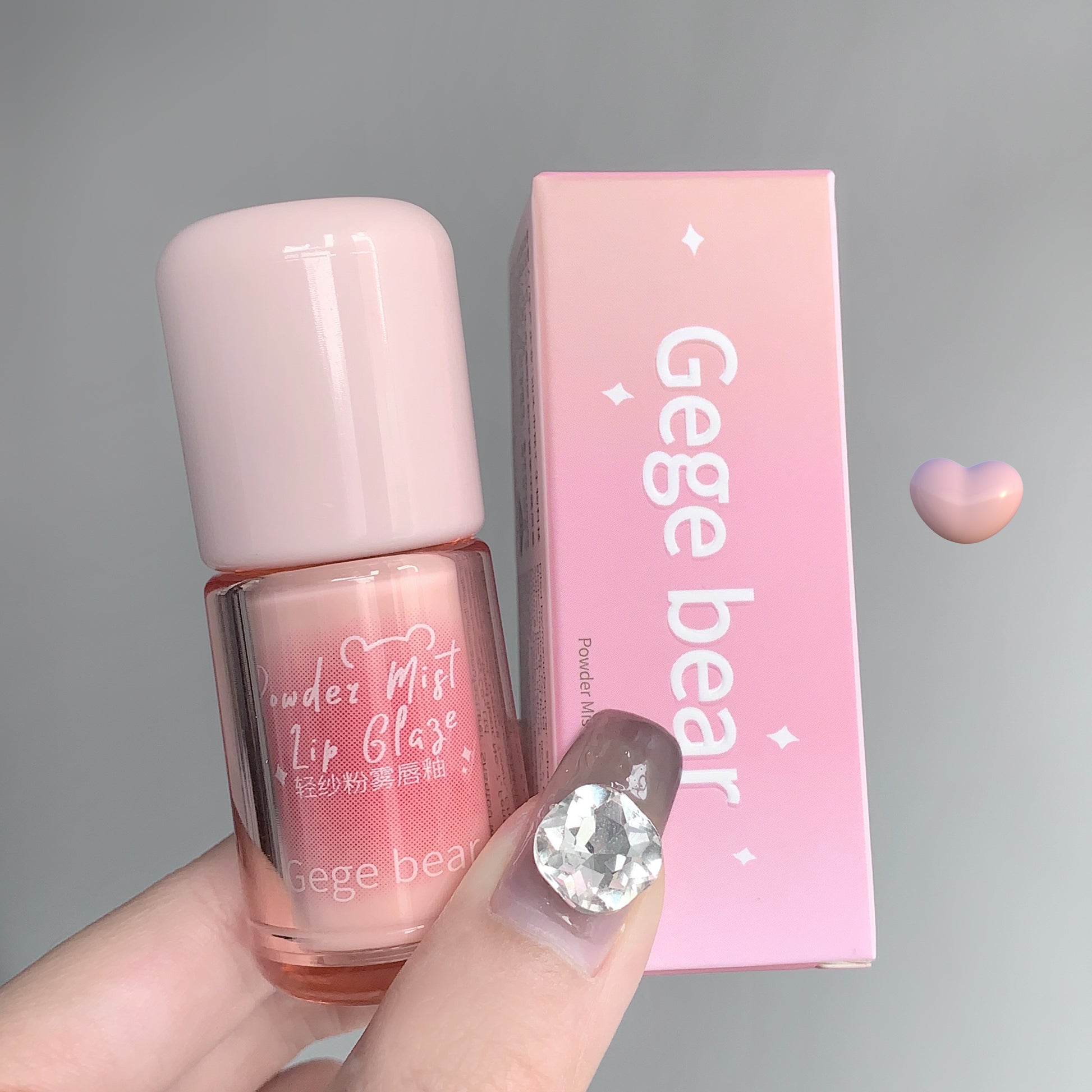 Pink lip gloss with 'Gege bear' branding held by a hand against a gray background