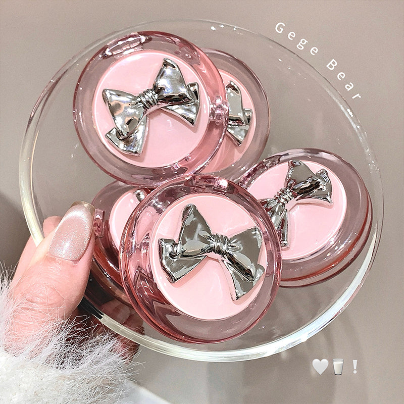 Pink compact mirrors with silver bows held by a hand on a neutral background