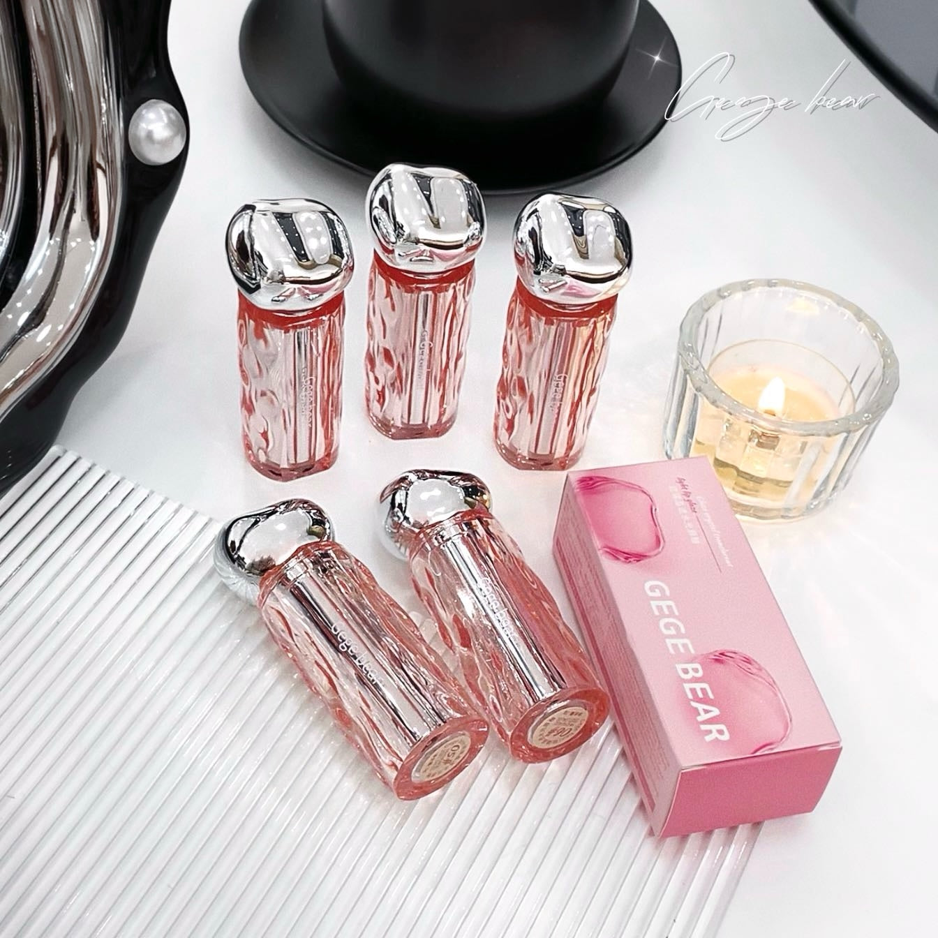 Pink and silver lip glosses with a pink box on a white surface.
