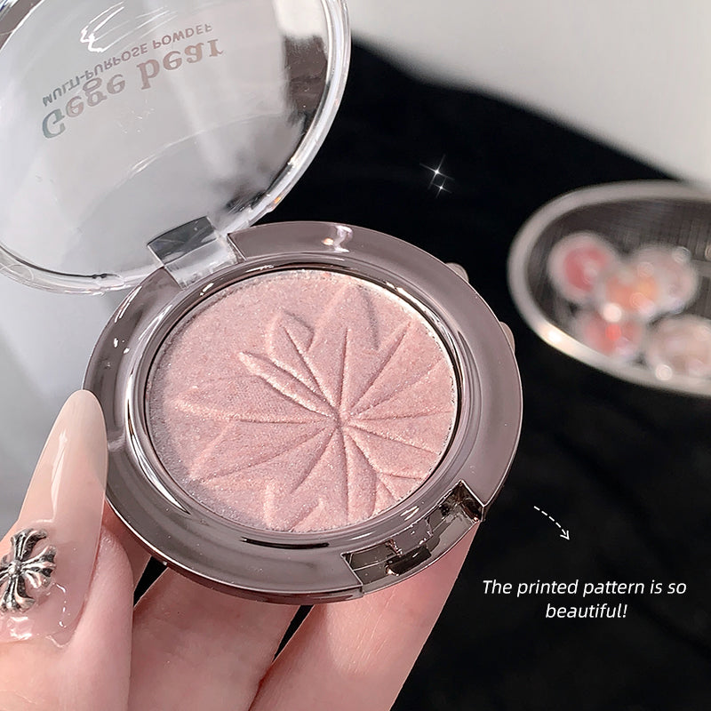 Compact powder with a decorative pattern held by a hand, with another compact in the background.