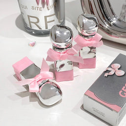 Silver perfume bottles with pink bows on a white surface