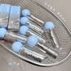 Clear lip gloss tubes with blue caps on a metal tray, branded 'Gege Bear'.