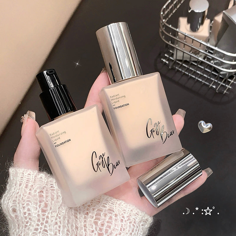 Two foundation bottles held by a hand with a blurred background