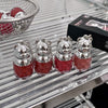 Four small bear-shaped containers with red liquid on a metallic surface.