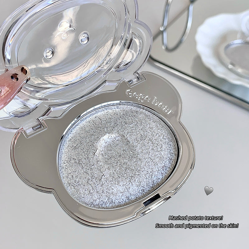 Compact powder with silver textured powder inside, on a light background.