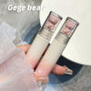 Two lip glosses with bear-shaped ends held by a hand, branded 'Gege bear'.