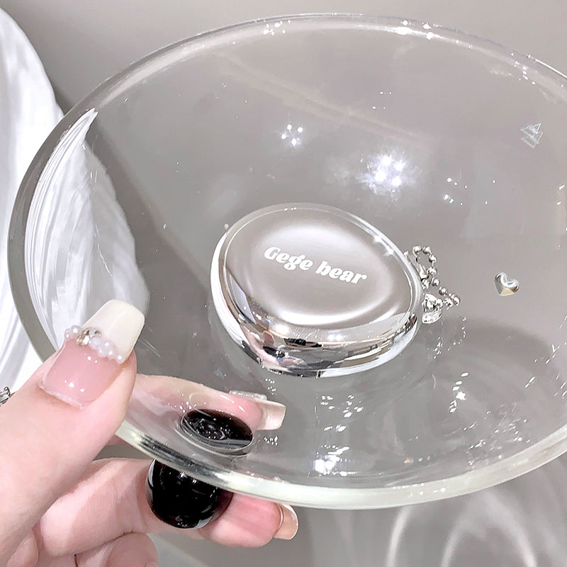 Clear glass lid with 'Gege bear' branding held by a hand against a neutral background