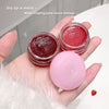 Hand holding two small containers of red lip balm and a pink sphere, with text about dry lips being moist.