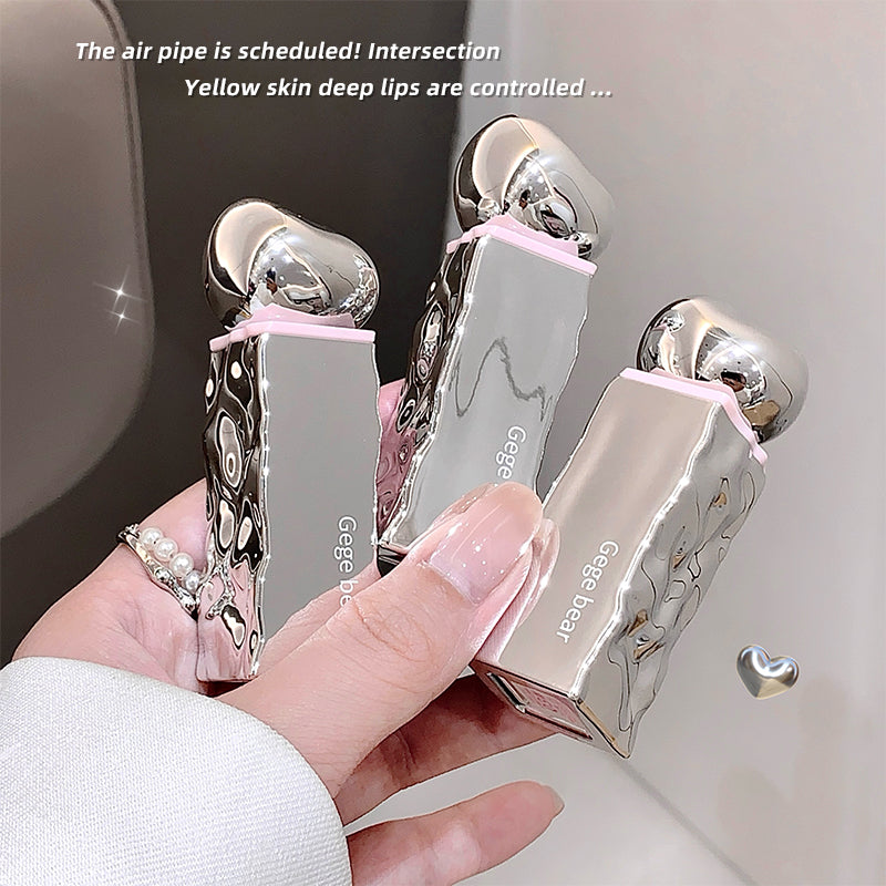 Three silver lip glosses with pink accents held by a hand against a neutral background