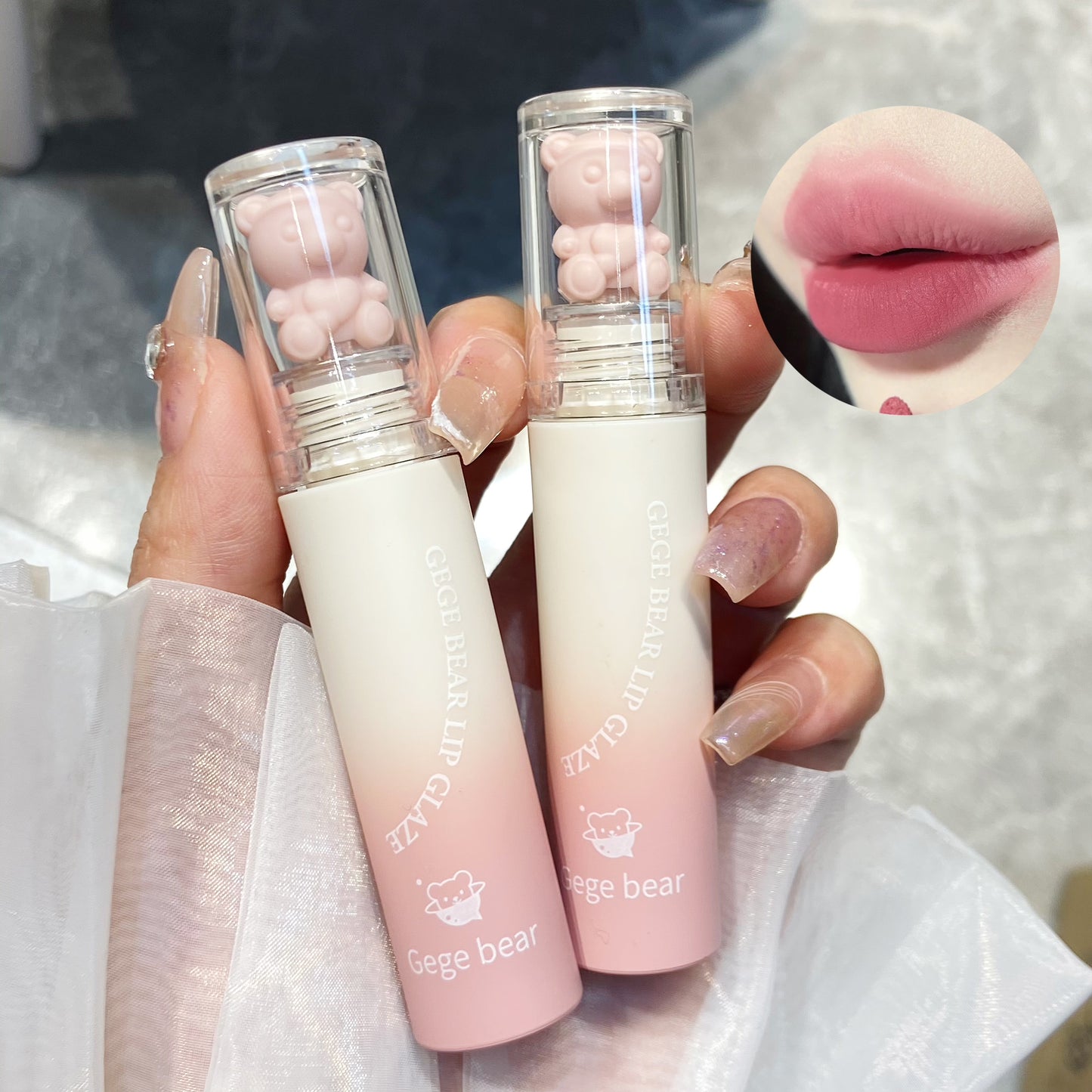 Two lip balms with bear-shaped caps held by a hand, close-up of lips shown.