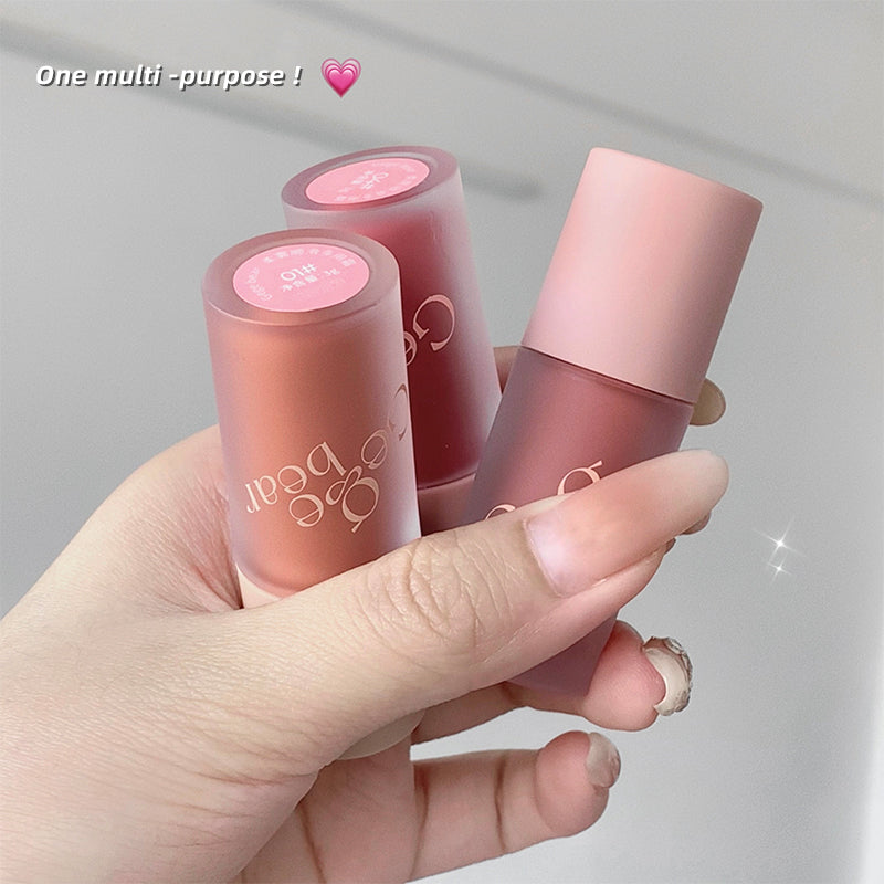 Three lip glosses with pink and nude shades held in a hand against a light gray background.