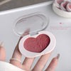 Heart-shaped blush compact held by a hand with a blurred background