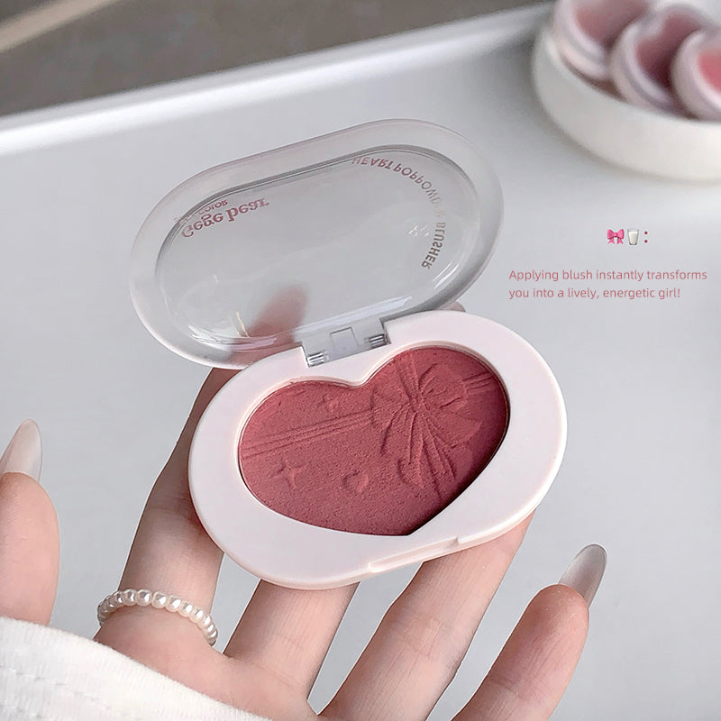 Heart-shaped blush compact held by a hand with a blurred background