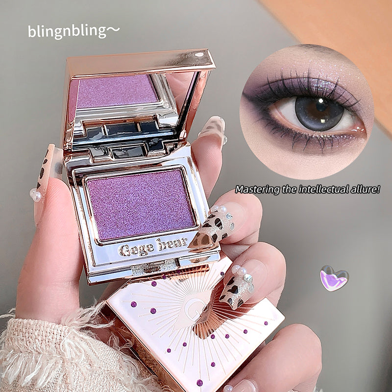 Purple eyeshadow compact held by a hand with decorative nails, showing an eye with purple makeup.