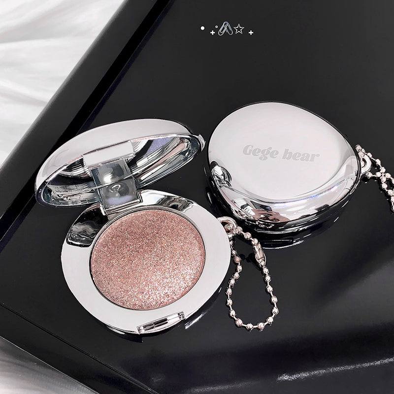 Makeup compact with pink glittery powder on a black surface, featuring the brand 'Gege bear'.