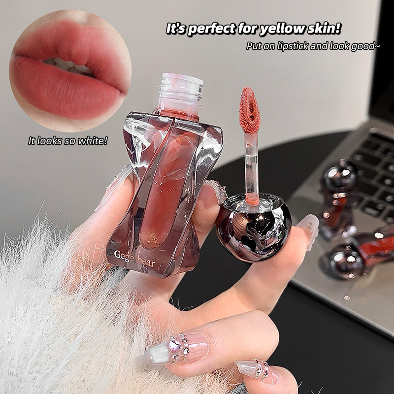 Lip gloss with applicator held by a hand, shown on yellow skin with text overlay.