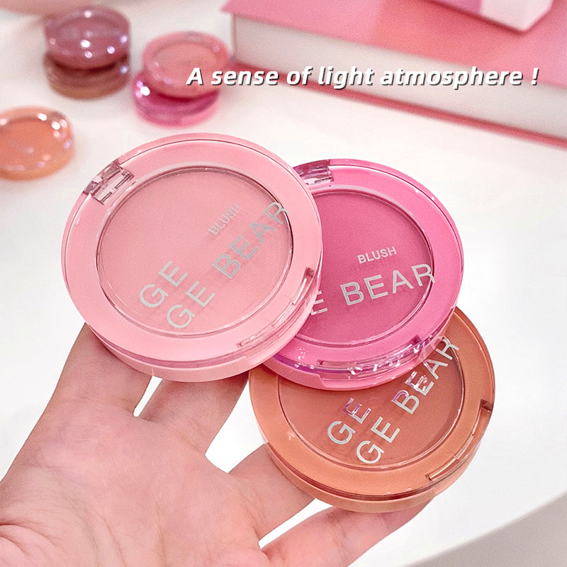 Three blush compact cases from the brand 'GE BEAR' held by a hand on a light pink background.