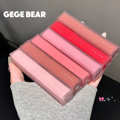Set of Gege Bear lip glosses held by a hand against a dark background