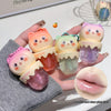 Hand holding four small, colorful lip gloss containers with cartoon designs on a light background.