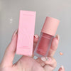 Hand holding a pink multi-purpose cream with its packaging against a gray background