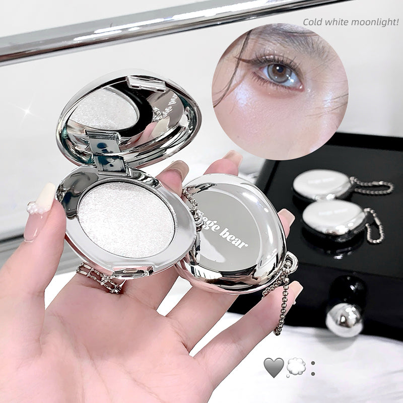 Compact mirror with decorative chain held by a hand, showing close-up of eye with product application.