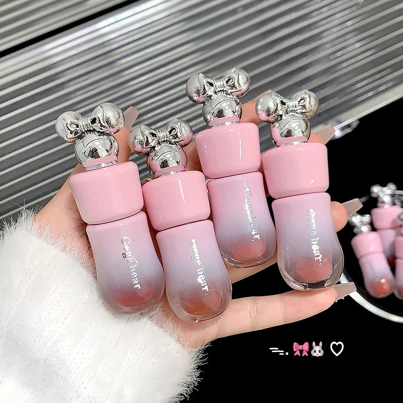 Set of pink gradient lip balms with silver tops held by a hand against a metallic background.