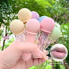 Set of colorful lip balms held by a hand with a blurred green outdoor background