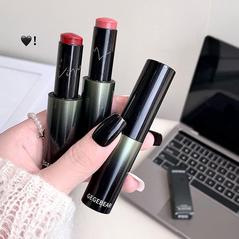 Hand holding three lipsticks with 'GEGEBEAR' branding in front of a laptop.