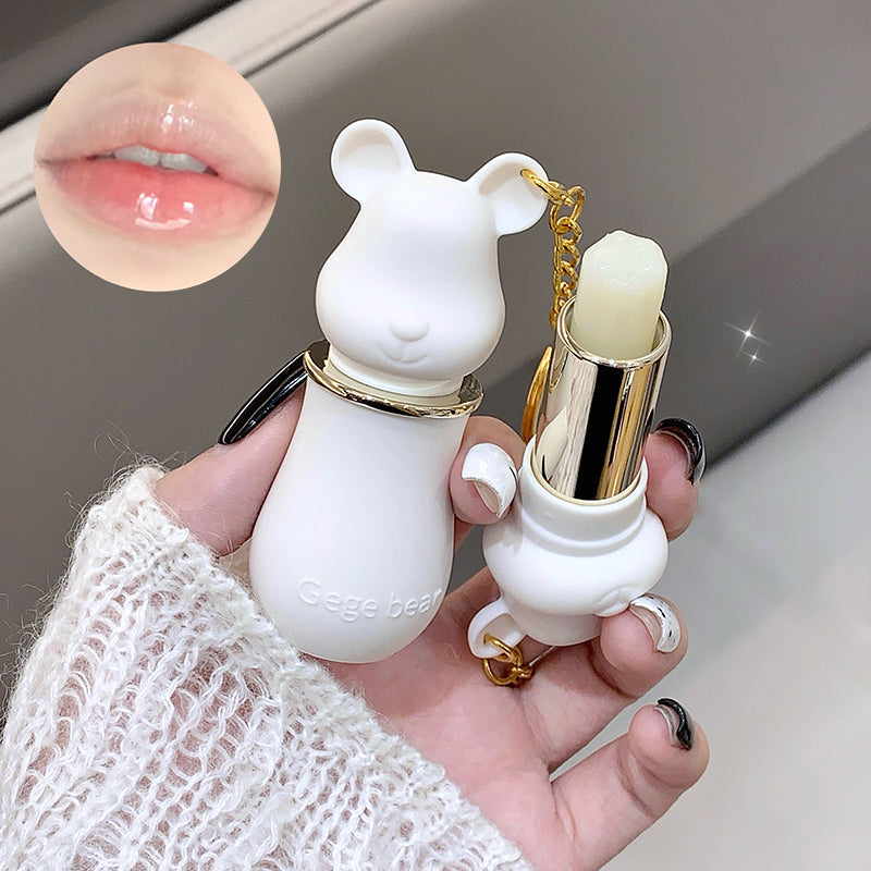 White rabbit-shaped lip balm with gold accents held by a hand, close-up of lips shown.